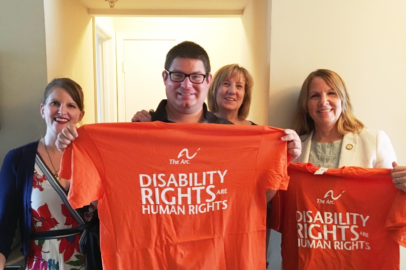 one male self advocate and three women pose holidng orange T-shirts that read 