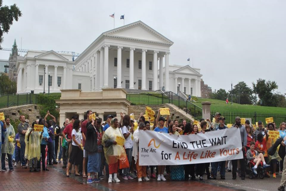 a large group of self-advocates gathers in front of the Virginia capital building, holding a banner that reads 