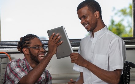 one young black man shows another young black man the screen of a tablet.