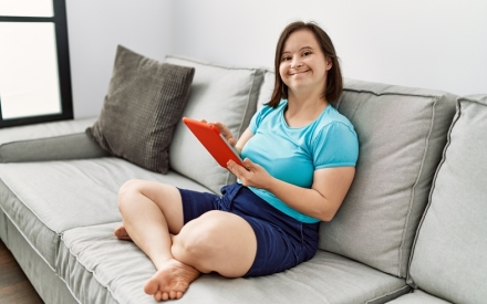 young adult woman with IDD sits on the sofa in her apartment holding a tablet