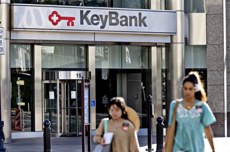 Photograph of an office building showing a revolving door, and a sign for Key Bank over the door. Two women walk by the building in the foreground