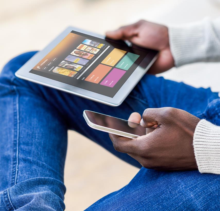 close up photo of a black man wearing jeans and a white sweater, he holds a smartphone in his left hand, and an iPad in his righ hand. the iPad shows the Arc 2 independence app on the screen.