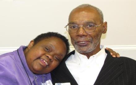a close-up headand shoulders photo of an aging black man, and his adult child with a disability leaning her head on his shoulder.