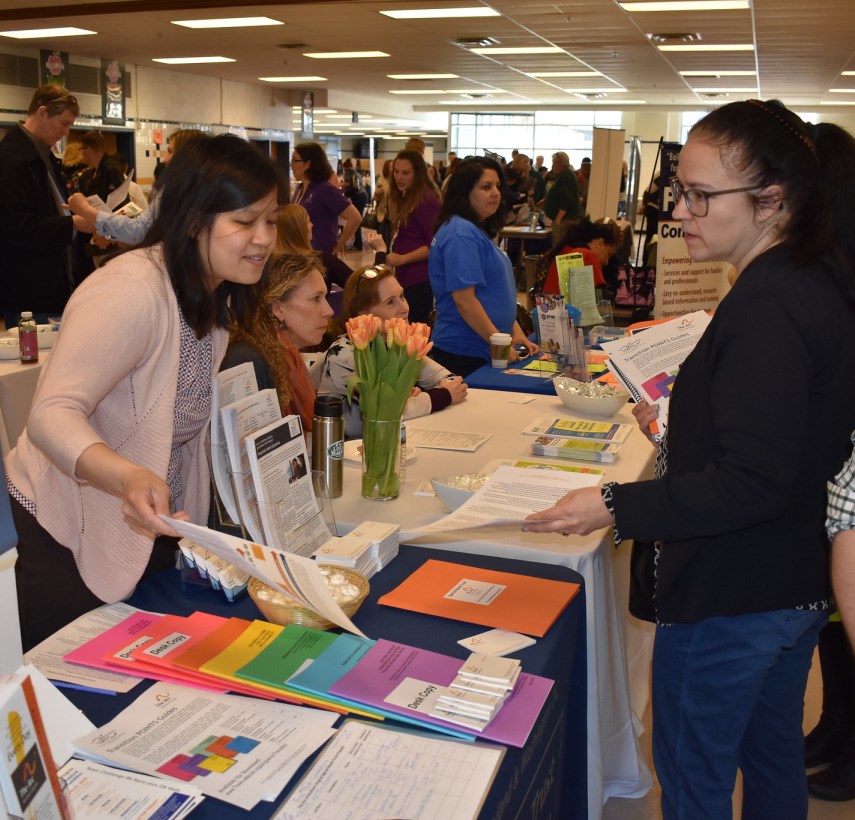 staff member Lisa Fong leans over a table of guide books and fliers to talk with a woman attending the resource fair.