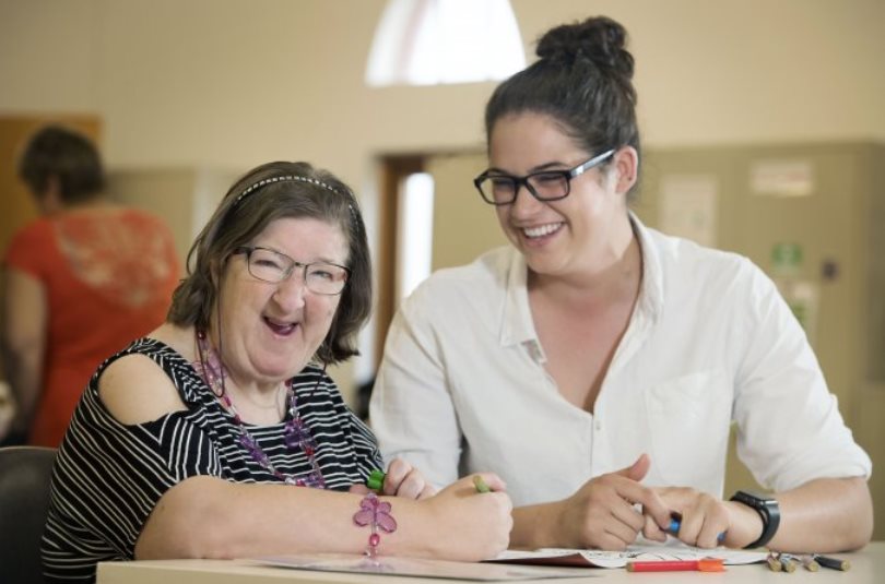 a middle aged woman with developmental disabilities sits at a table next to another woman who is her support coordinator