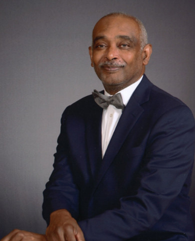 seated photo of Michael Thomas, wearing a dark blue suit coat over a white shirt and a bowtie
