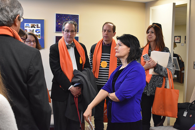 A group of advocates from The Arc, each wearing an orange scarf, speak with State Senator Favola in the hallway of the legislative office building in Richmond.
