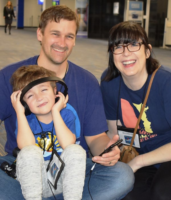 Young boy with autism clutches his headphones, while sitting on the floor with dad and mom sitting behind him