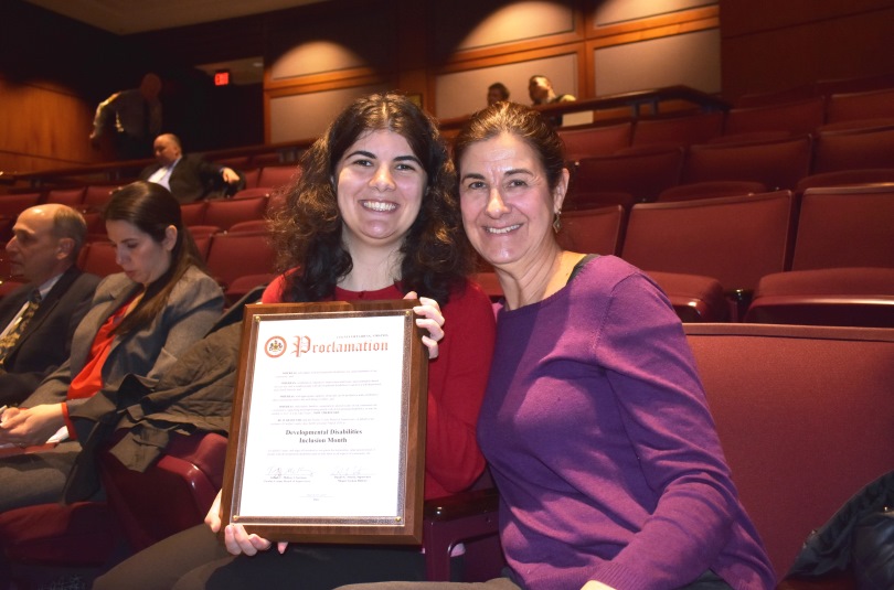 young woman and her mother pose in an auditorium holding a proclamation for DD Awareness Month