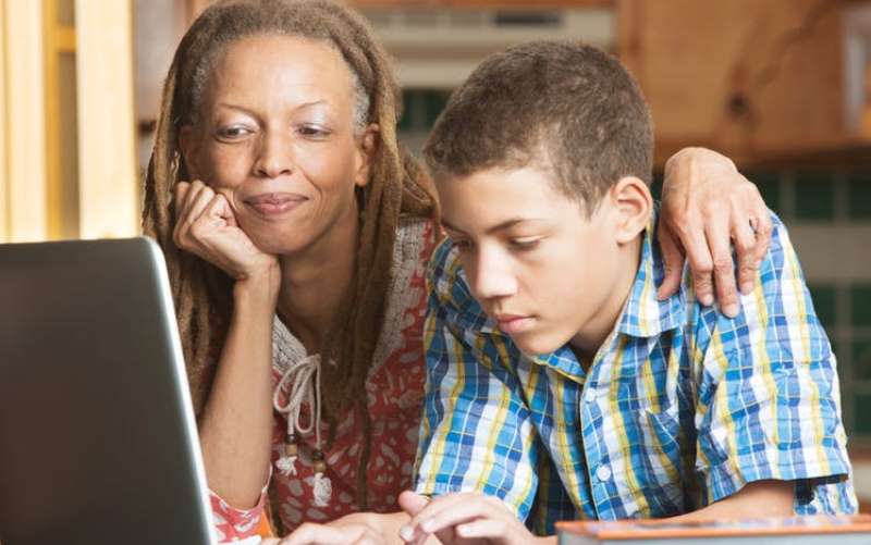 African American mother and pre-teen son gaze at a laptop computer. Mom has her chin resting on one hand, and her other arm around her son's soulders.