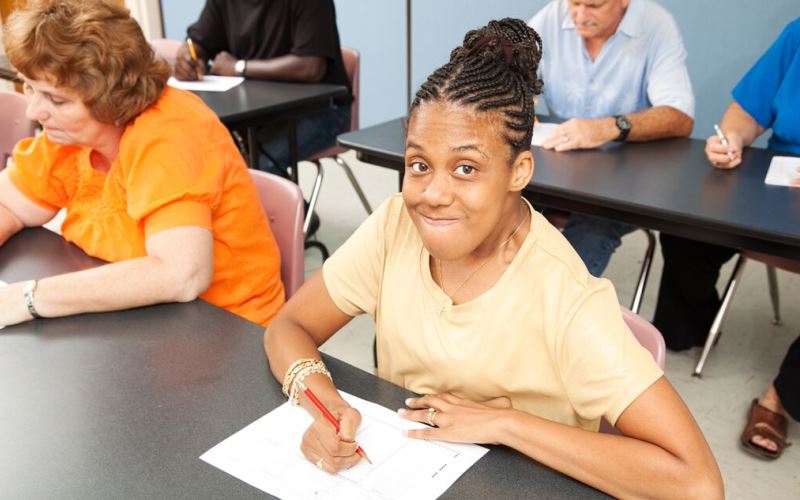Female African American college student looks at the camera while sitting at a table filling out a form.