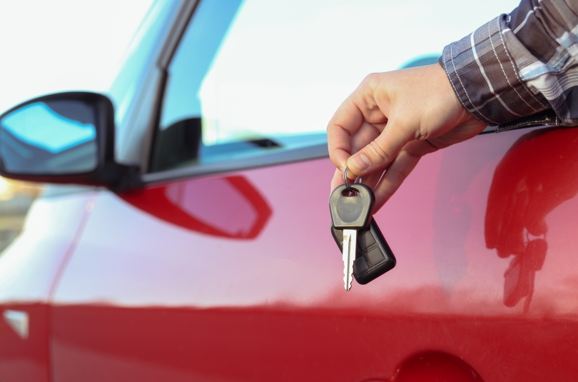 close up photo of a mans hands holding a car key dangling out the window of a red car
