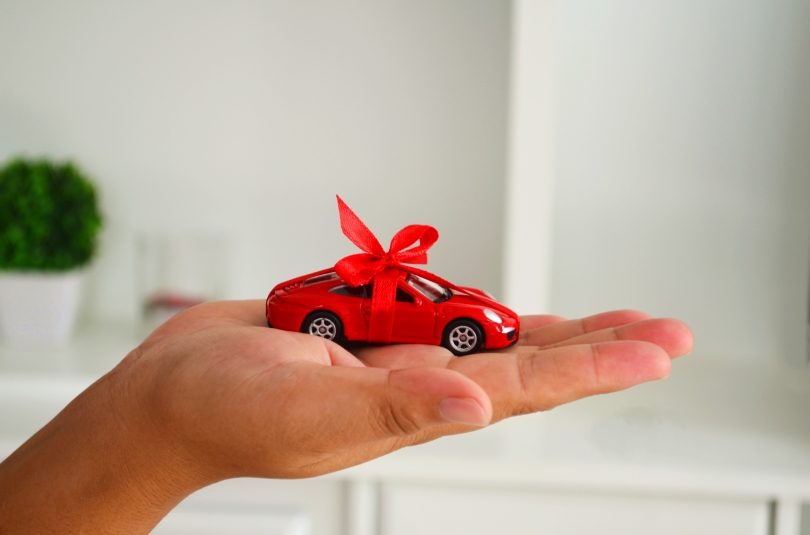 photo of a woman's hand, palm up, holding a red toy car with a red bow on it.