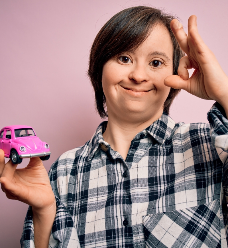 Young woman with IDD giving the OK sign with her left hand, and holding a pink toy car in her right hand