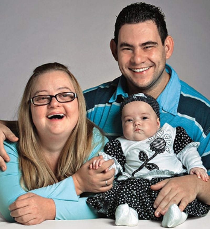 A young married couple with developmental disabilities pose with their baby daughter.
