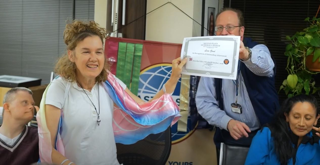 a woman with IDD stands to receive a certificate of achievement from a group facilitator