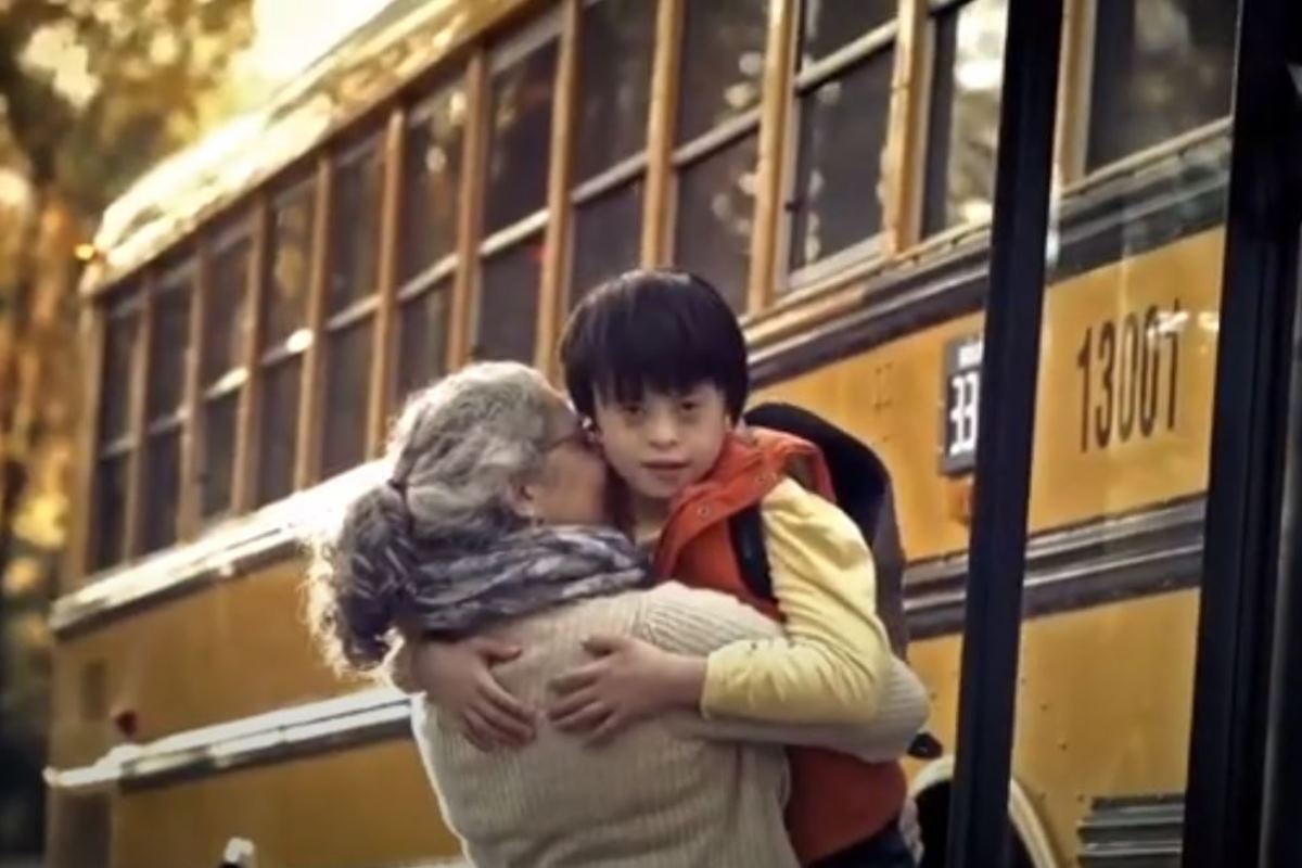 A young Asian boy is helped off a school bus by his grandmother.