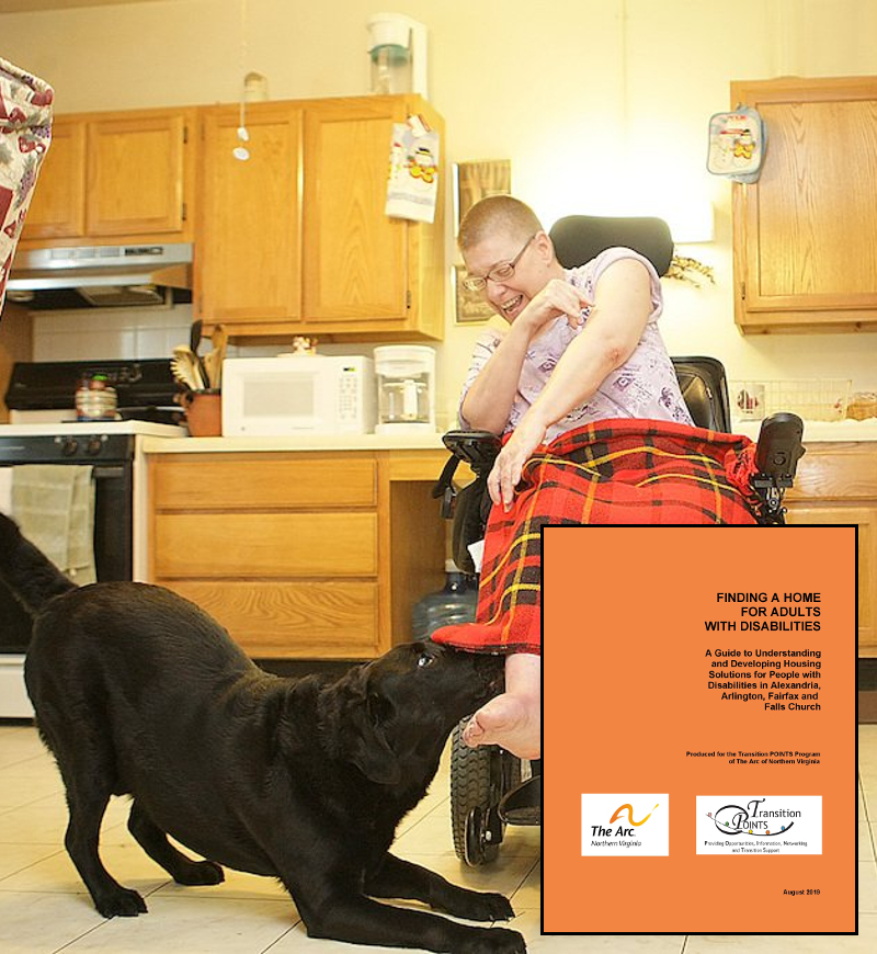 A young adult male sits with a plaid blanket covering his legs in his wheelchair in the kitchen of his home. he is playing with a black lab dog who crouches beside the man.