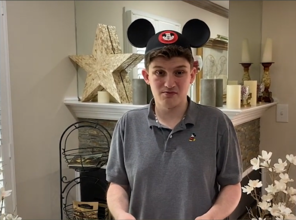 head and shoulders photo of Conner Cummings, looking directly at the camera. Conner is in his living room, wearing a gray polo shirt and Mickey Mouse ears.