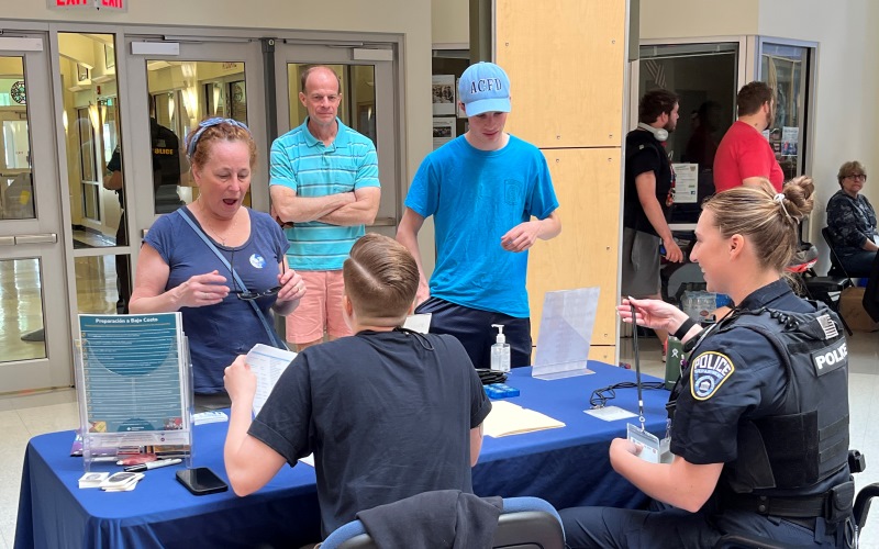 a young adult male with autism and his parents are greeted at the event by a police officer sitting behind a table.